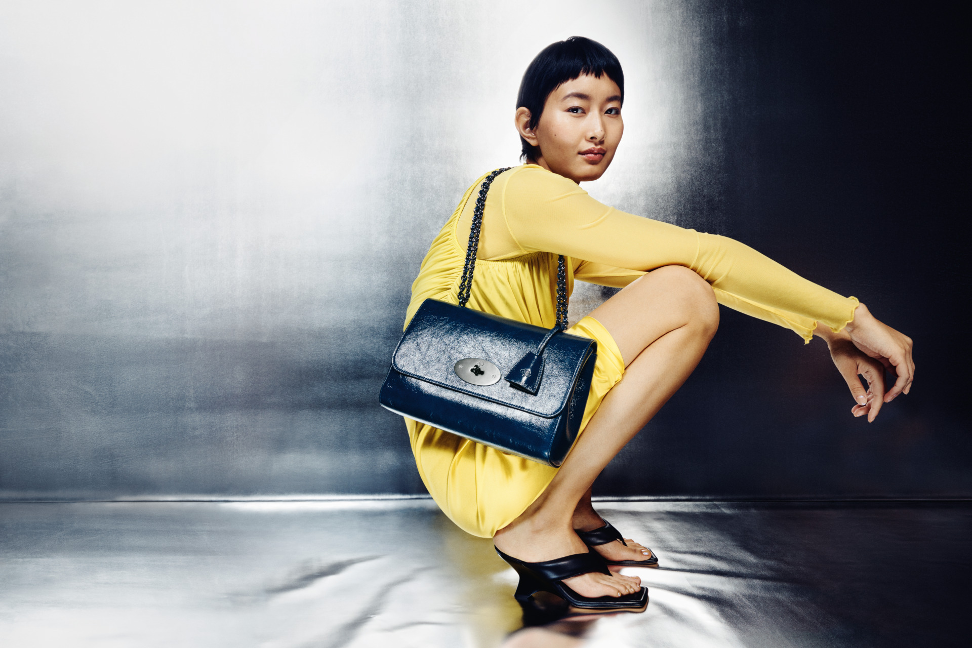 Woman crouched wearing yellow dress and black bag