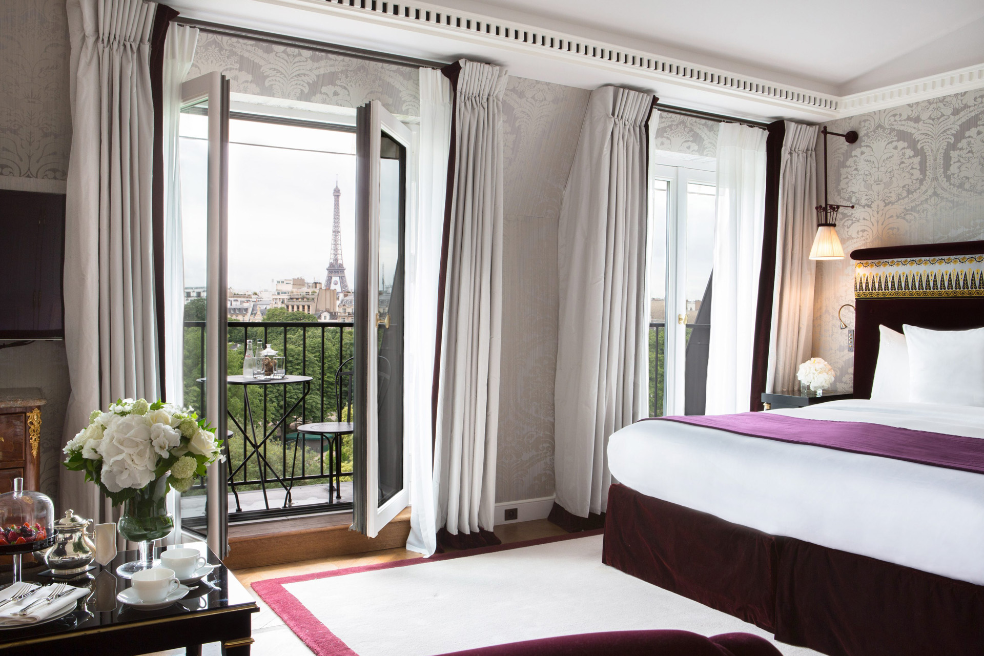 A bed with French doors opening onto a balcony with the Eiffel Tower in the background