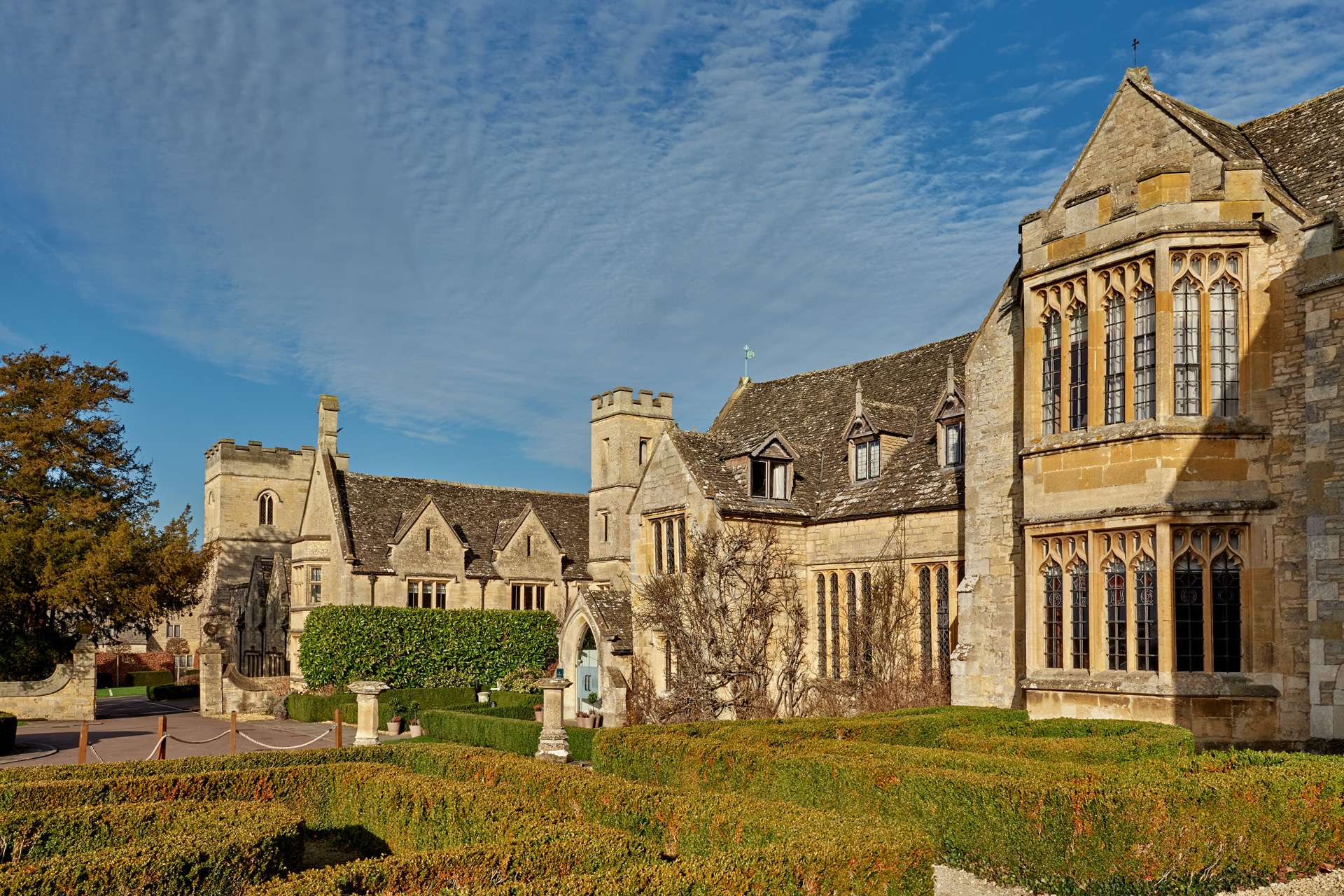 Exterior of Ellenborough Park Hotel, with sandstone brick buildings and landscaped hedges in the foreground.