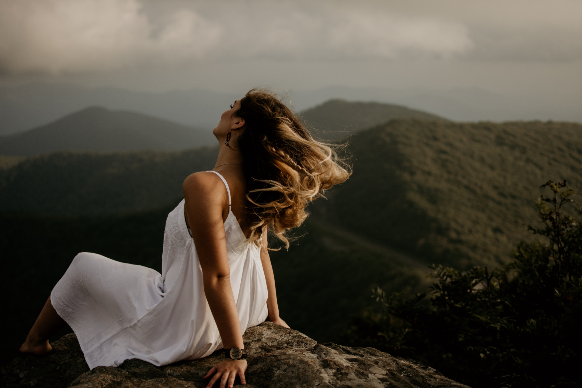 Woman in white dress sat on rock overlooking mountainous landscape