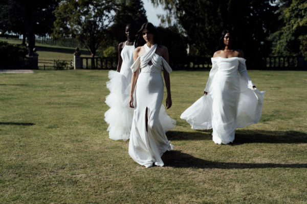 Three women in wedding dresses walking across grass
