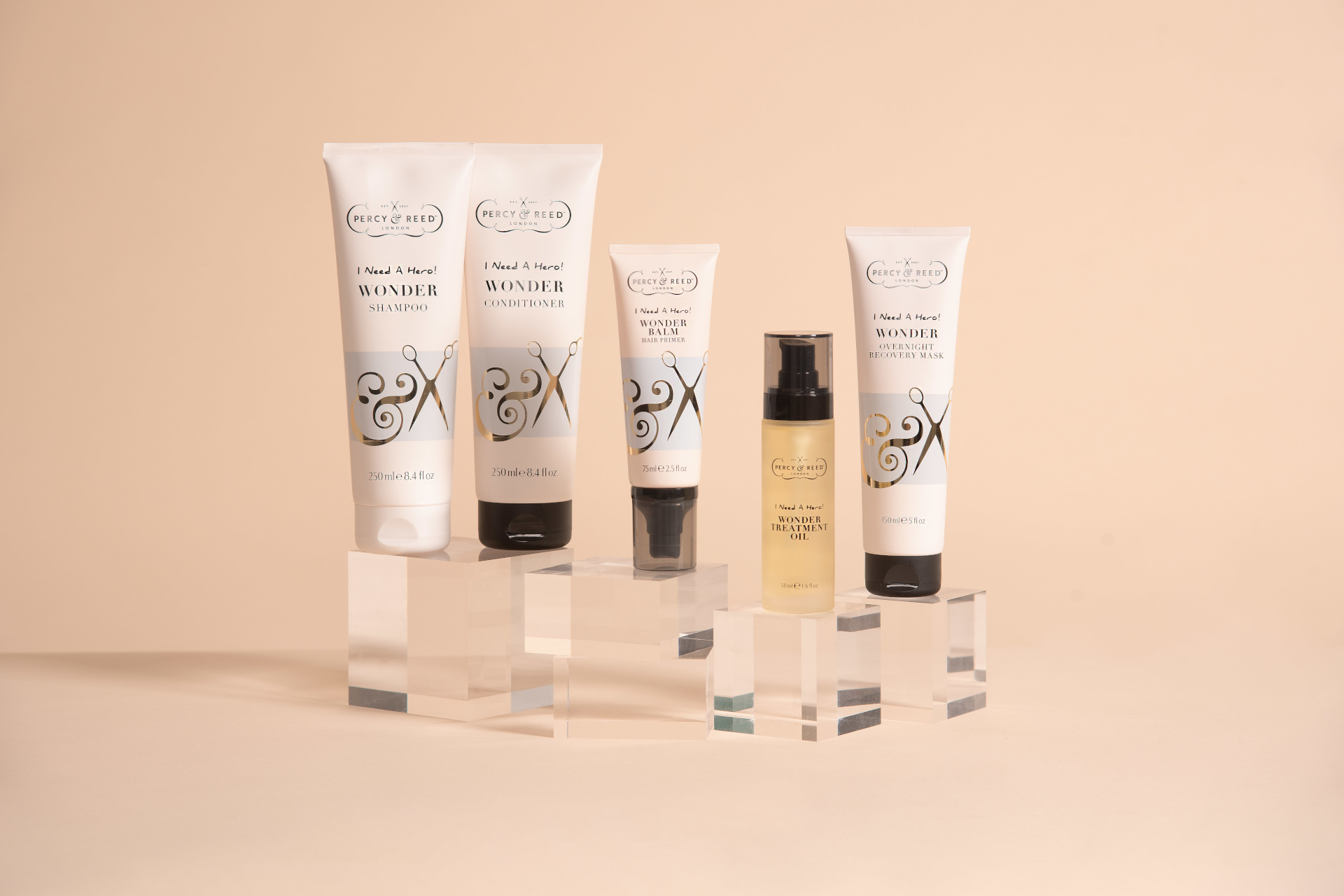 Hair products lined up of glass boxes in front of pink background