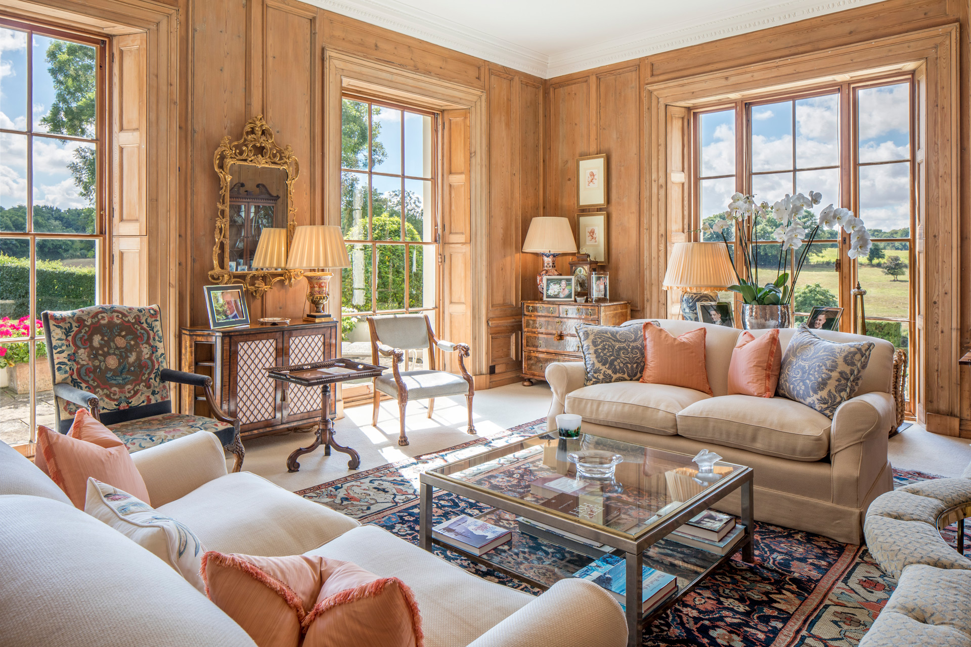 Wood-panelled living room with cream sofas, orange cushions, glass coffee table and views of the hills.