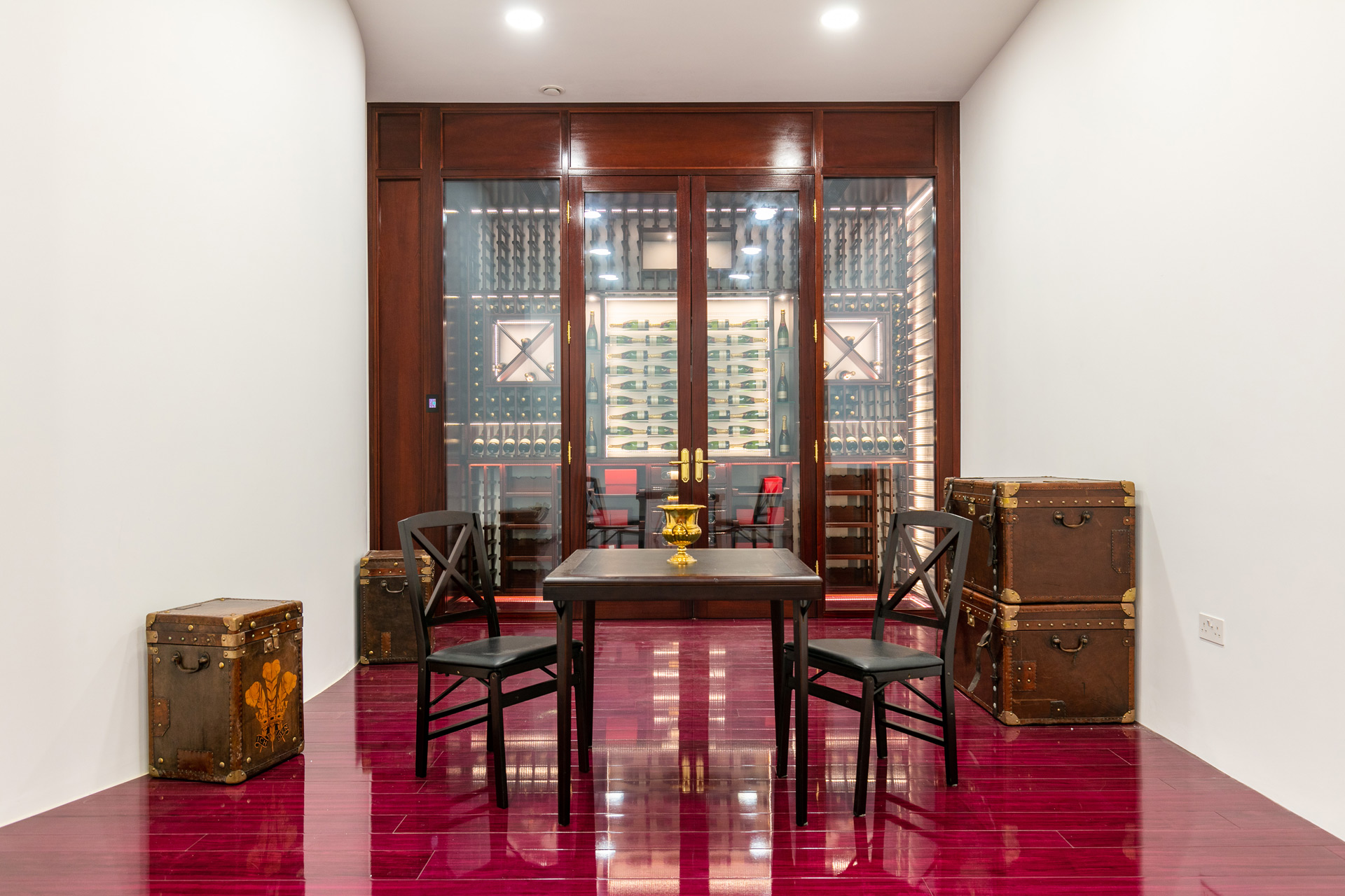 Cellar with old-fashioned trunks, varnished red floor, and glass cases of wine.