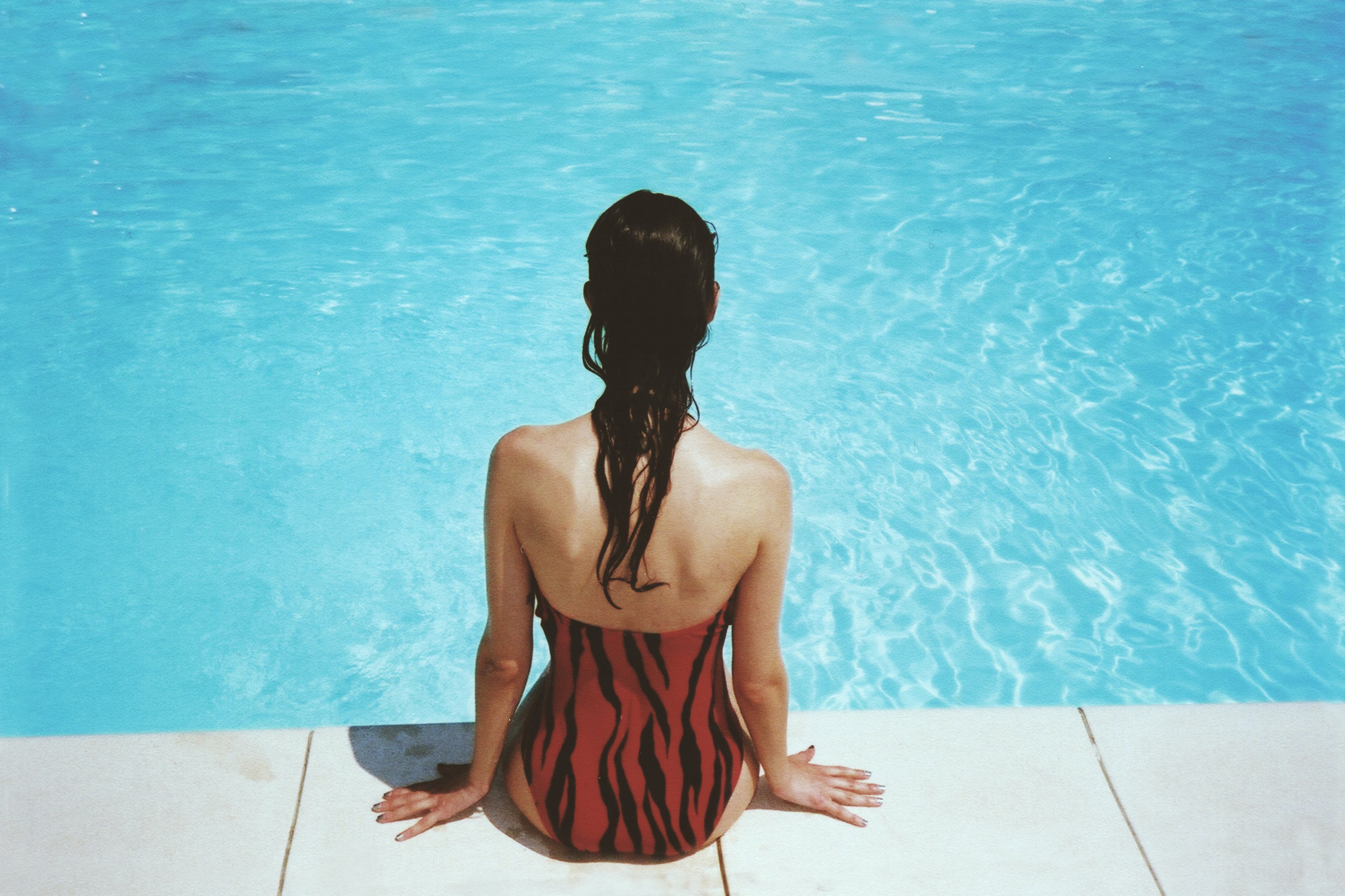 Woman in swimsuit sitting on the edge of a swimming pool.