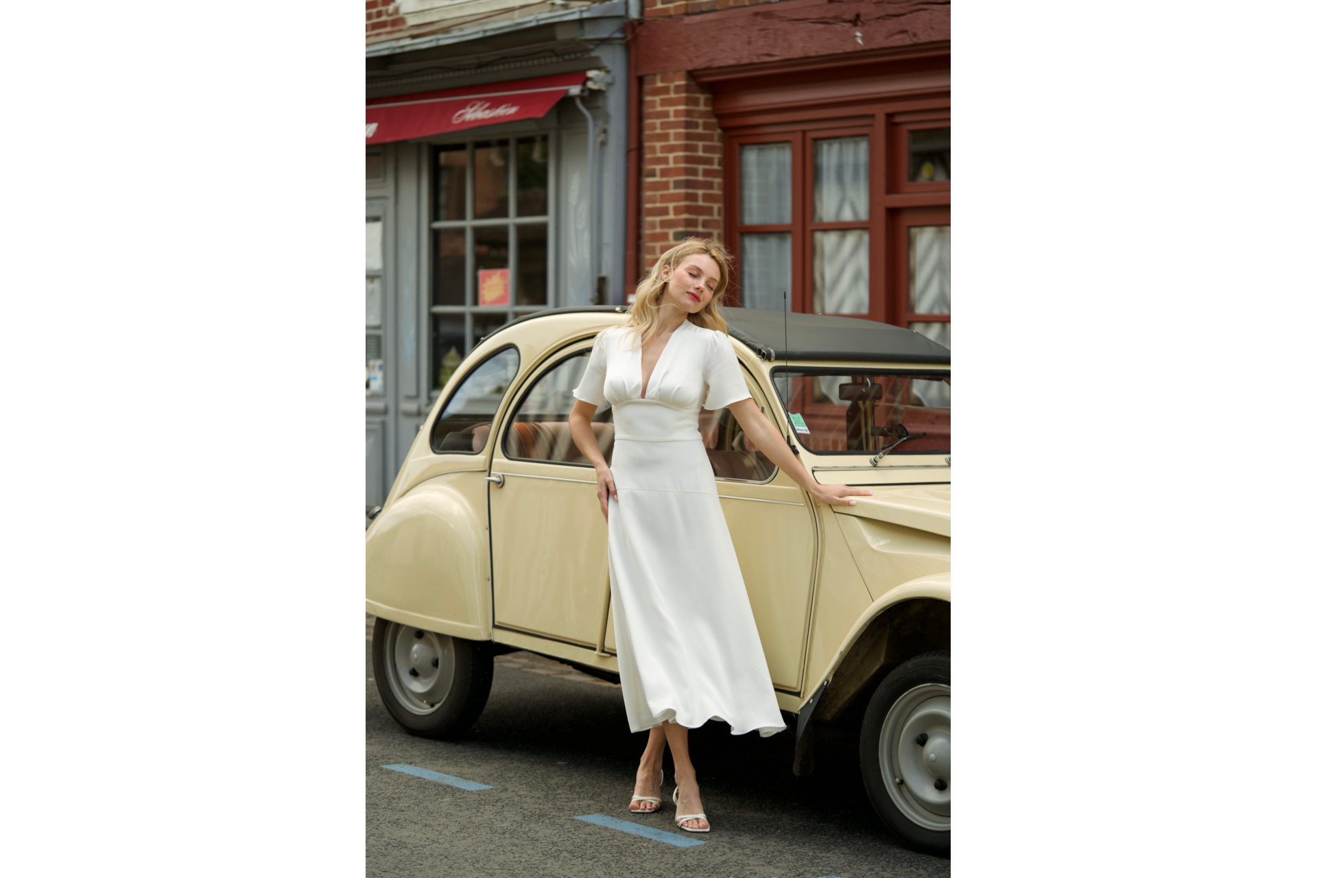 Woman stood in front of pastel yellow car in white dress