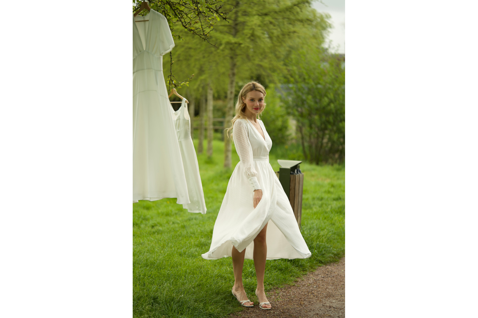 Woman in white dress stood in field with white dresses hung on branches