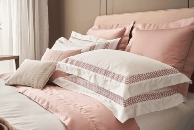 White bed linen with light pink-bordered pillows, a pink runner and pink cushions.